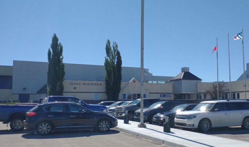 Plan large sur l'école Beauséjour de Plamondon, lors d'une journée ensoleillée. De nombreuses voitures sont présentes dans le stationnement.