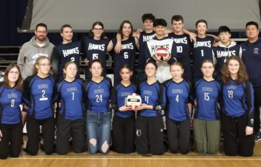 Des jeunes en uniformes de sport posent pour une photo, avec leurs entraîneurs à leurs côtés.