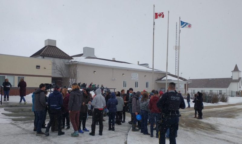 Les élèves de l'école Beauséjour sont amassés devant l'école, avec les drapeaux canadien et franco-albertain flottant au vent.