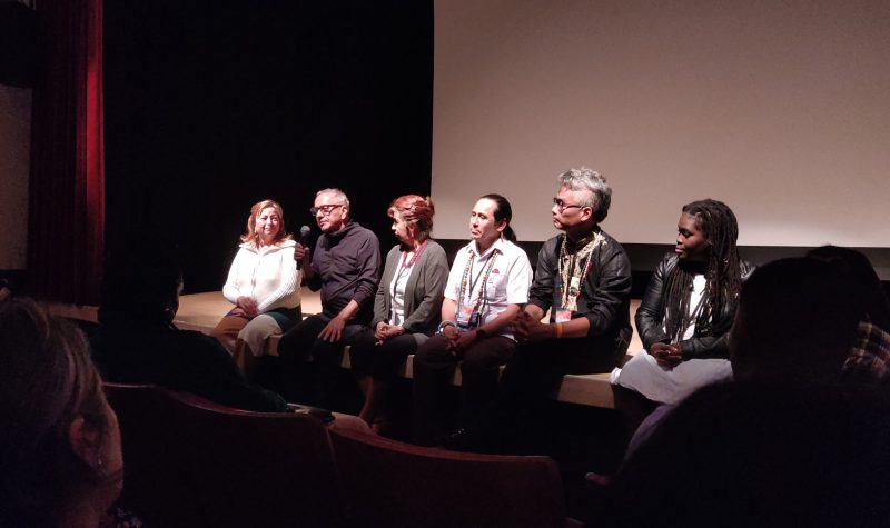 seis personas sentadas en el piso del escenario de un teatro/cine