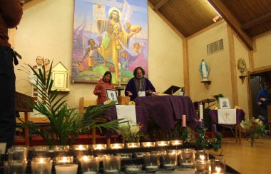 velas encendidas en una capilla y dos personas rezando al fondo