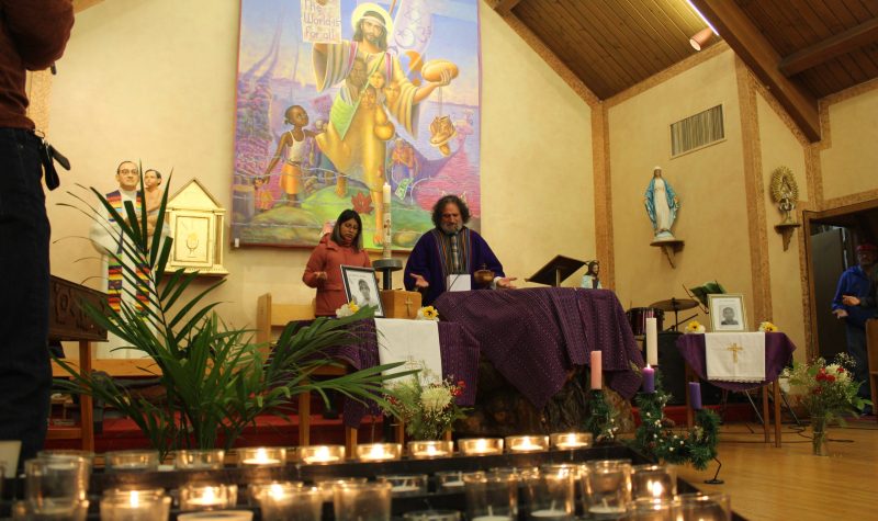 velas encendidas en una capilla y dos personas rezando al fondo