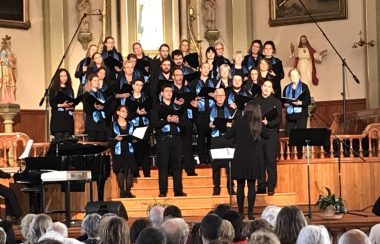 Un groupe de personne sur la scène en formation chorale écoutant leur chef