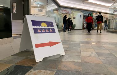 Une pancarte sur le sol d'un centre d'achat, avec le drapeau TliCho et une grande flèche rouge, indique la voie vers le bureau de vote