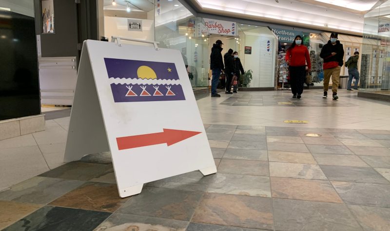 Une pancarte sur le sol d'un centre d'achat, avec le drapeau TliCho et une grande flèche rouge, indique la voie vers le bureau de vote