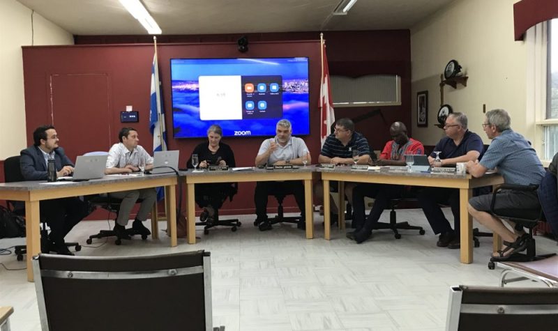 Les membres du conseil assis dans une salle équipée d'un téléviseur