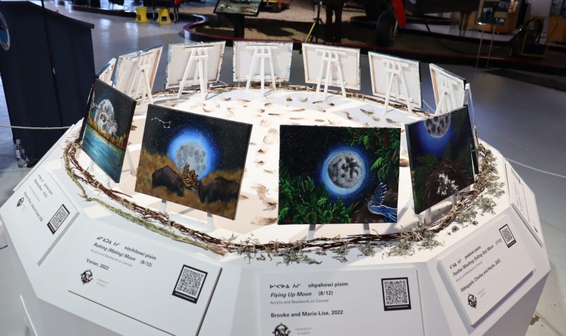 ê-pimihâyahk (we are all flying together) exhibit at ALberta Aviation Museum. It is a small circular white table with 12 paintings featured in a circle.