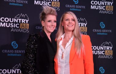 Amy Heff and Darya Fitsko stand in front of a banner displaying the Country Music Alberta Awards logo, along with their main sponsor, on the red carpet.