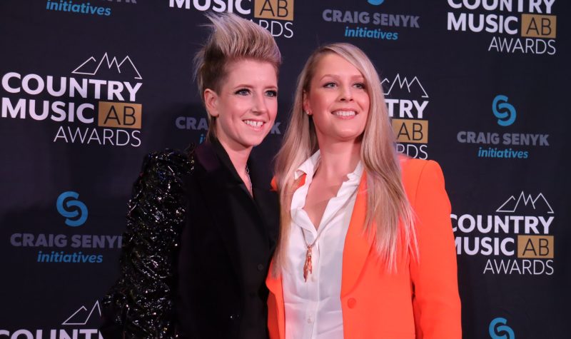 Amy Heff and Darya Fitsko stand in front of a banner displaying the Country Music Alberta Awards logo, along with their main sponsor, on the red carpet.