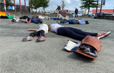 Half a dozen people lay sprawled across a the tiles of a city squre