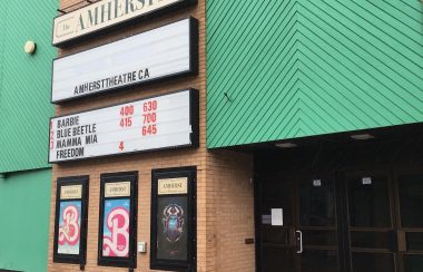 The front of a building with a sign saying Amherst Theatre with a list of movies.