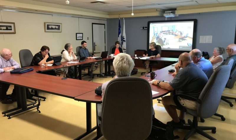 Une dizaine de personnes assis à une table de conférence dans une salle avec écran