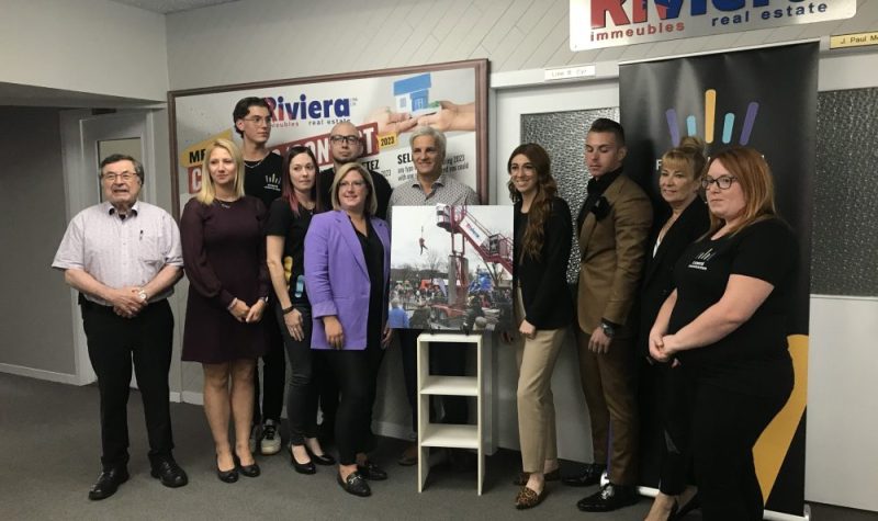 Neuf personnes prenant la pose autour du visuel de la tyrolienne.