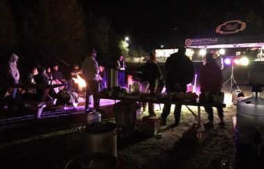 Un groupe de personnes à l'extérieur en fin de soirée autour d'un feu