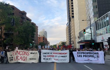 Protestors hold up three banners decrying Bill 31 while hundreds walk behind them on Sherbrooke Street in Montreal, Quebec.