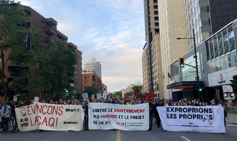 Protestors hold up three banners decrying Bill 31 while hundreds walk behind them on Sherbrooke Street in Montreal, Quebec.