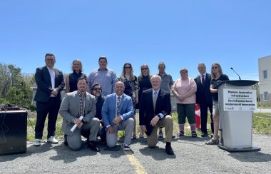 Total of 13 board members and provincial officials are standing and smiling for a picture behind the community building.