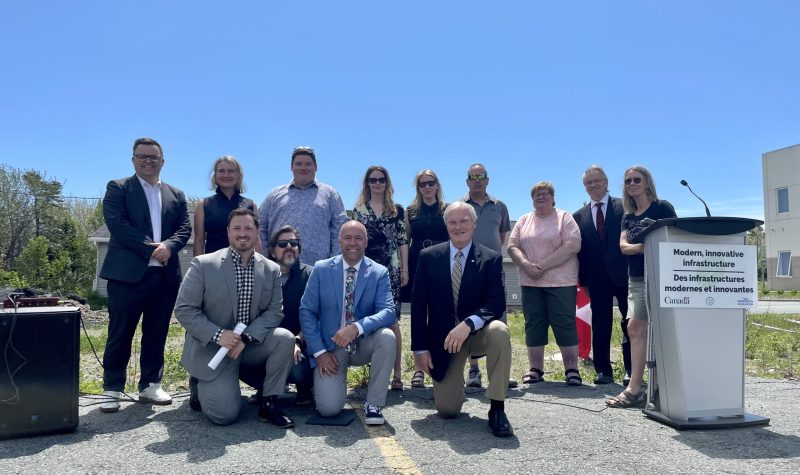 Total of 13 board members and provincial officials are standing and smiling for a picture behind the community building.