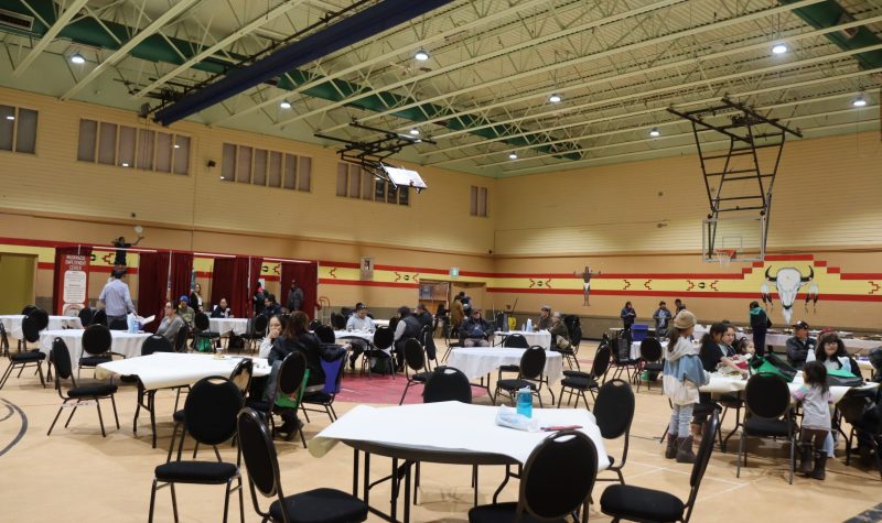 A gymnasium full of chairs and roundtables as people eat lunch and listen to the speakers at the front of the room. There are also water agencies with booths in the back of the gym.