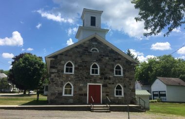 Pictured is the Olivet Church that CAB Sutton is currently in the midst of renovating. It is a small fieldstone church with a red door.