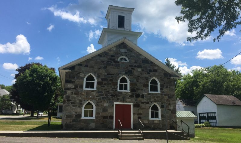 Pictured is the Olivet Church that CAB Sutton is currently in the midst of renovating. It is a small fieldstone church with a red door.