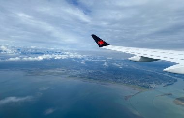 Vue aérienne de l'océan et d'une ville côtière, sous des nuages blancs, captée du hublot d'un avion, vis-à-vis de l'aile.