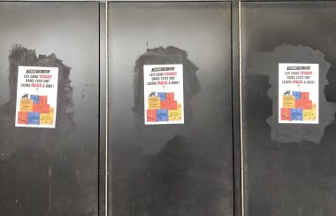Three protest posters decry the unaffordability of housing on a set of doors to the Olympic Stadium in Montreal.