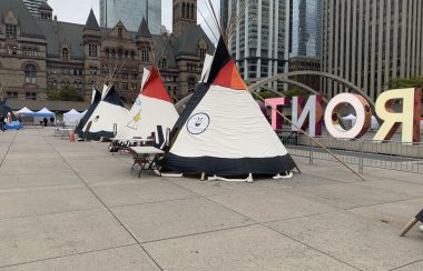 Tipis of different colours outside with a sign and building behind them.