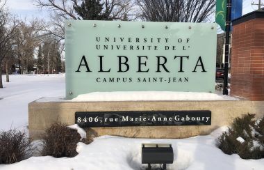 Enseigne du campus Saint-Jean. Les lettres sont écrites en noires et le fond du panneau d'affichage est blanc. Il est inscrit Université de l'Alberta Campus Saint-Jean. Le mot Alberta est écrit en caractère plus gros.