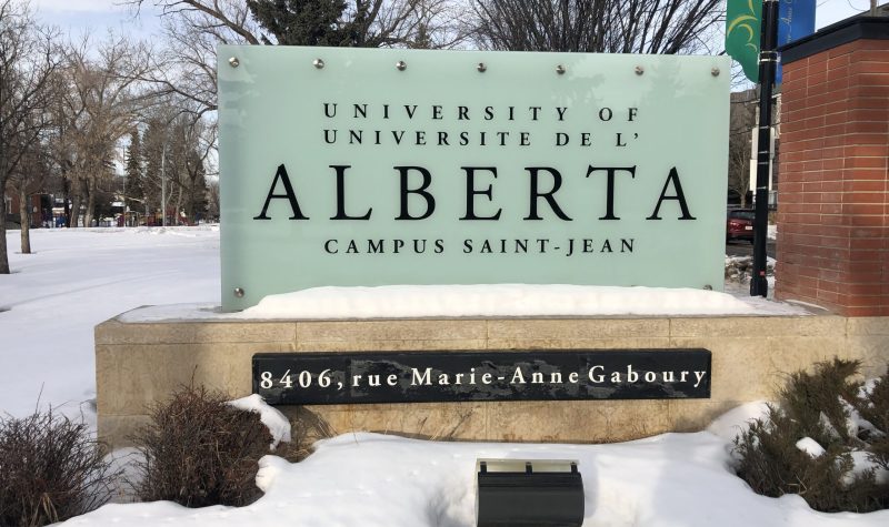 Enseigne du campus Saint-Jean. Les lettres sont écrites en noires et le fond du panneau d'affichage est blanc. Il est inscrit Université de l'Alberta Campus Saint-Jean. Le mot Alberta est écrit en caractère plus gros.