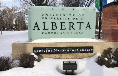 Panneau d'indication du campus Saint-Jean de l'Alberta. Les écritures sont en noires et le panneau est blanc. Le mot Alberta est plus gros en taille que les autres mots. Le panneau indique Université de l'Alberta Campus Saint-Jean.