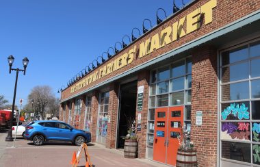 The front of the Old Strathcona Farmers Market as seen from the street. Weather is sunny and clear.