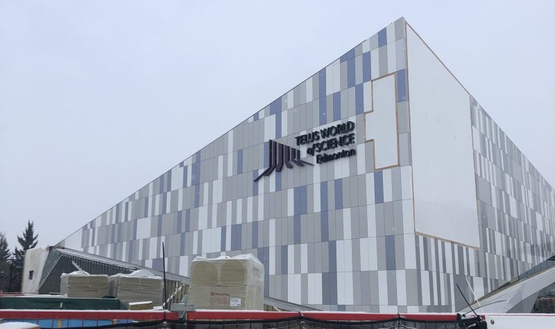 Édifice du Centre de sciences Telus d'Edmonton. Les tuiles sur la façade de l'édifice sont de couleurs bleues, grises et blanches. Les tuiles forment des rectangles. Devant la façade, il est inscrit Telus World of science Edmonton