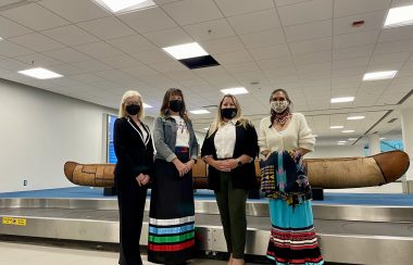 All three guest speaker and the elder who said prayers during the ceremony. There is a 19 foot canoe behind them.