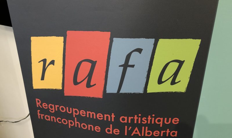 Affiche du Regroupement artistique de l'Alberta. L'affiche est de couleur noire et un carré encadre chaque lettre du nom. La lettre R est encadré d'un carré jaune, la lettre a est encadré d'un carré rouge, la lettre F est encadré en bleu et l'autre lettre A est encadré en vert.
