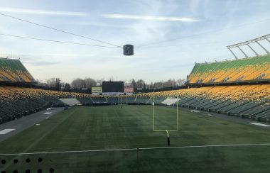 Vue sur le terrain de football du stade Commonwealth à Edmonton. On aperçoit le terrain de gazon synthétique et les estrades de couleur verte et jaune.
