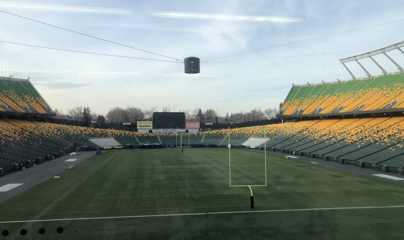Vue sur le terrain de football du stade Commonwealth à Edmonton. On aperçoit le terrain de gazon synthétique et les estrades de couleur verte et jaune.