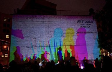 Des projections de couleurs des silouettes de gens dans la rue contre un mur.