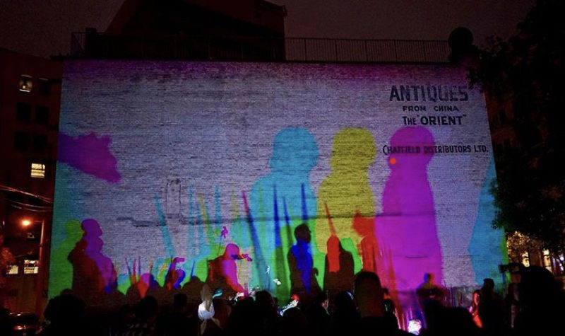 Des projections de couleurs des silouettes de gens dans la rue contre un mur.