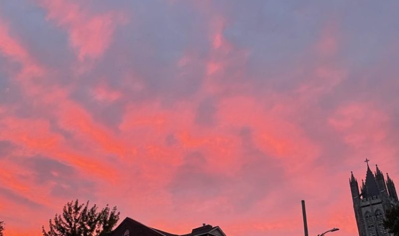 sunset in kingston, the upper portion of the image is taken up by the sky, which is various shades of red, pink, and some grey-ish clouds. A large house and the top of a church is visible in the lower half of the frame