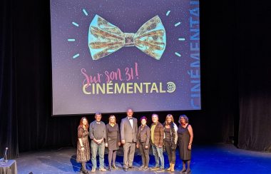Le président de l'organisation Cinémental, Henri Dupuis, debout au milieu avec de nombreuses autres personnes autour de lui posant devant un grand écran qui indique qu'il s'agit du 31ème festival de films.
