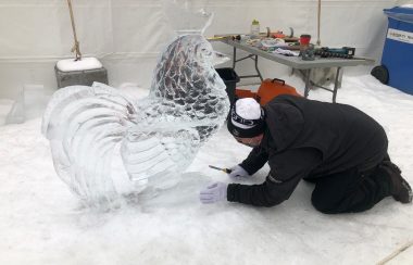 An ice sculptor hard at work, finishing up a carving of a chicken in purely clear ice. Weather seems fair.