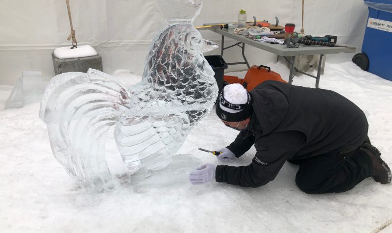 An ice sculptor hard at work, finishing up a carving of a chicken in purely clear ice. Weather seems fair.