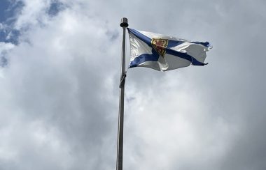 Photo of the Nova Scotia flag. There are clouds in the background.