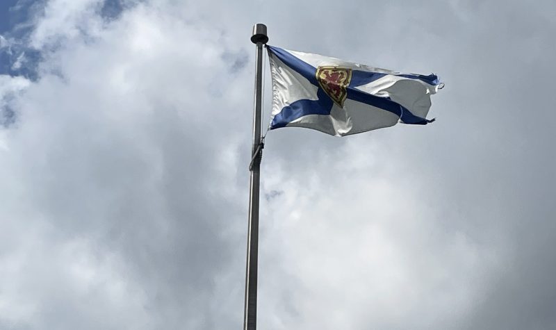 Photo of the Nova Scotia flag. There are clouds in the background.