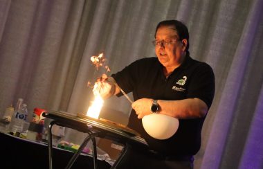 A presenter stands on a stage holding a balloon full of pure oxygen, and a candle in the other. He lets the balloon go over the candle, causing the flame to go up.