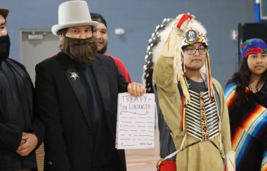 A small theatrical performance features youth dressed up as people from the government as well as Alexis Nakota Sioux Nation signing Treaty 6. The photo was taken inside a gymnasium.
