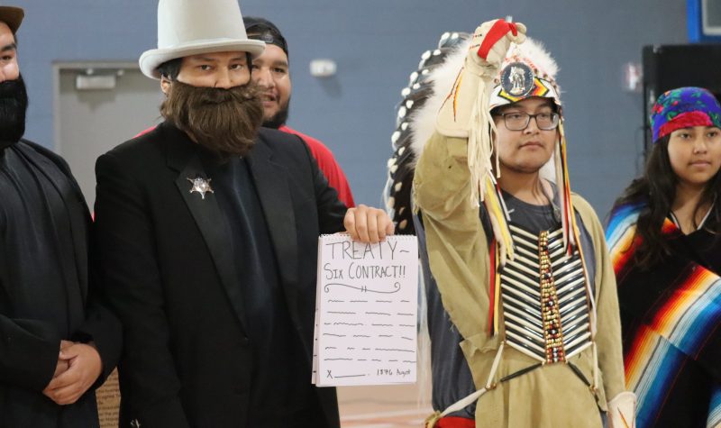 A small theatrical performance features youth dressed up as people from the government as well as Alexis Nakota Sioux Nation signing Treaty 6. The photo was taken inside a gymnasium.