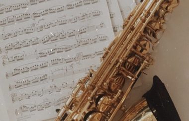 Close up of a saxophone on a table with sheet music underneath it.