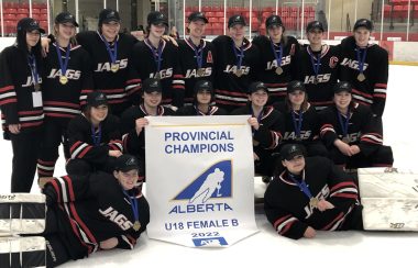 The 2022 U18 Provincial Champions Lakeland Jaguars posing in front of their championship banner at center ice.